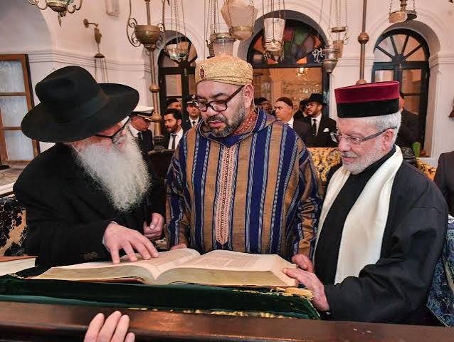 King Mohammed VI of Morocco examining a religious manuscript alongside a rabbi and a religious official in a Moroccan synagogue — a photograph that expresses the personal commitment of the Moroccan royal house to the preservation of the country's Jewish heritage